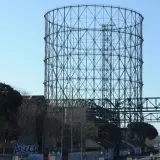 Il **gasometro Roma** si erge imponente contro il cielo azzurro, una struttura metallica iconica che domina il paesaggio urbano.