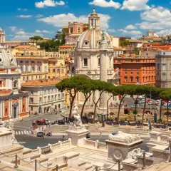 Vista panoramica di Roma con l'Altare della Patria in primo piano, cupole imponenti e palazzi storici sotto un cielo azzurro con nuvole bianche.