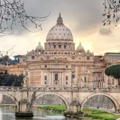 Un ponte di Roma attraversa il Tevere, con la maestosa cupola di San Pietro che domina lo skyline in una giornata invernale.
