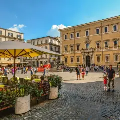 Piazza animata con gente che passeggia e si gode la movida a Roma, tavolini all'aperto e palazzi storici sullo sfondo.