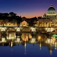 Ponte Sant'Angelo illuminato di notte, con la cupola di San Pietro sullo sfondo. Un'idea per cosa visitare a Roma in due giorni.