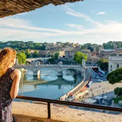 Una donna ammira il panorama di Roma con il Tevere e Ponte Sant'Angelo, un'immagine perfetta per il Ferragosto a Roma.
