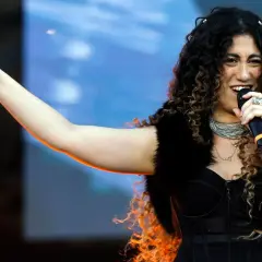 Una delle tanti artisti primo maggio, canta con passione sul palco, indicando il pubblico con un gesto energico.