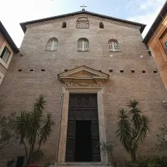 Facciata in mattoni di Santa Prassede a Roma, con un grande portale in legno e piante verdi.