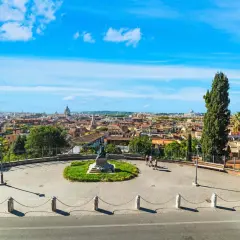 Vista panoramica di Roma con cupole e tetti, un monumento al centro e persone che passeggiano. Un'emozione da vivere a Roma gratis.
