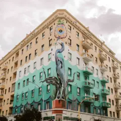 Un maestoso airone blu e tentacoli di polpo adornano un palazzo nel quartiere Ostiense, un'opera d'arte urbana che cattura lo sguardo.