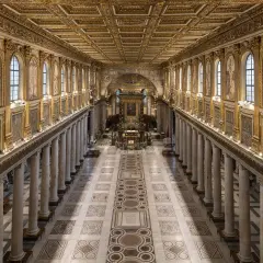 L'interno della Basilica di Santa Maria Maggiore a Roma, con il suo soffitto dorato, le colonne imponenti e i mosaici che narrano storie sacre.
