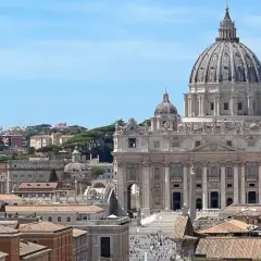 Vista panoramica di Roma con la Basilica di San Pietro in primo piano. Si intravedono i tetti della città e il cielo azzurro. Vicino alla stazione Ottaviano, un luogo iconico.