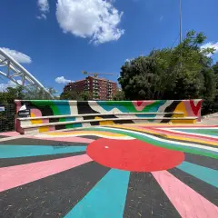 Piazza colorata vicino alla metro Garbatella a Roma, con un murale vivace e un grande sole stilizzato sul pavimento.