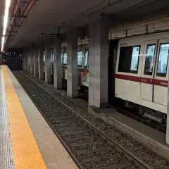 Persone attendono il treno alla stazione metro a Lepanto. Un convoglio bianco e rosso è fermo sui binari.