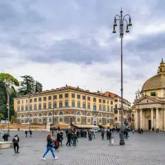Piazza del Popolo a Roma a novembre, con la chiesa gemella e il palazzo giallo sotto un cielo nuvoloso.