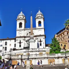 La scalinata di Trinità dei Monti a Roma, con la chiesa e l'obelisco sotto un cielo azzurro.