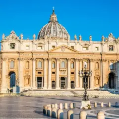 La maestosa basilica di San Pietro, un'antica meraviglia architettonica, domina la piazza con la sua imponente cupola sotto un cielo azzurro.