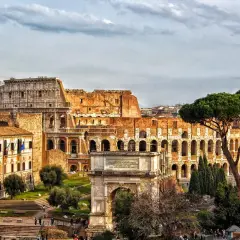 Colosseo e Arco di Tito, un'idea di cosa vedere a Roma in un giorno gratis, con pini romani e cielo nuvoloso.