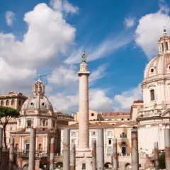 La colonna di Traiano si erge maestosa a Roma, con cupole barocche e pini marittimi sotto un cielo azzurro e nuvoloso.
