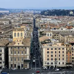 Vista aerea di Roma con traffico su Via del Corso. Edifici storici e tetti si estendono all'infinito.