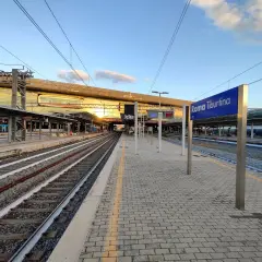 Binari e pensiline alla stazione Roma Tiburtina, con il sole che illumina la moderna architettura.