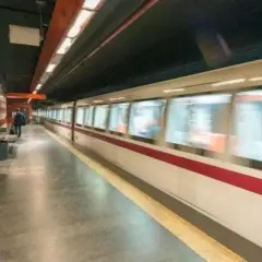 Treno in corsa su binari di una stazione metro. Si intravedono scale e un passeggero in attesa. Le fermate metro a Chiuse sono un luogo di passaggio frenetico.
