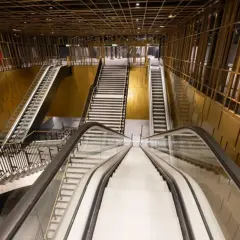 Interno moderno della **metro Cavour Roma**, con scale mobili e gradinate che conducono ai binari, pareti dorate e soffitto a griglia.