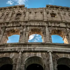 Il Colosseo visto dal basso, con il cielo azzurro e nuvole tra gli archi. Un'ottima meta per chi cerca come arrivare al Colosseo da Stazione Termini.
