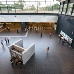 Interno moderno della fermata Teano metro C, con persone che acquistano biglietti e si dirigono verso i tornelli.