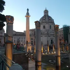 Antiche colonne onorarie illuminate di sera, con una cupola sullo sfondo.