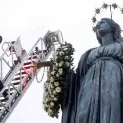 Vigile del fuoco su scala decora la statua della Madonna con fiori per l'8 dicembre a Roma.