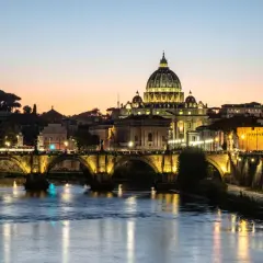 Ponte Sant'Angelo illuminato al tramonto, con Castel Sant'Angelo e la cupola di San Pietro. Un'idea su cosa fare il pomeriggio a Roma.