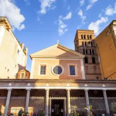 Facciata di San Lorenzo in Lucina a Roma, con il suo campanile romanico e palazzi circostanti sotto un cielo azzurro con nuvole bianche.