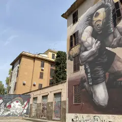 Street art a Tor Marancia: un imponente murale raffigura un lottatore con maschera tribale, mentre su un muro più basso un'altra opera celebra la cultura orientale.