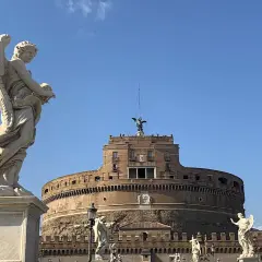 Un angelo scolpito domina la scena davanti al maestoso mausoleo di Roma, Castel Sant'Angelo, sotto un cielo azzurro.