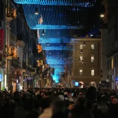 Folla festosa in strada a Roma, 25 dicembre, sotto luminarie blu e decorazioni natalizie.