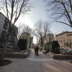 Passeggiata in un parco urbano, ideale per capire come arrivare a Testaccio da Termini. Alberi spogli, palazzi e persone con un passeggino.