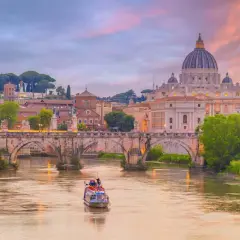 Tramonto su Roma con la maestosa chiesa San Pietro a dominare il paesaggio, mentre un battello naviga sul Tevere.