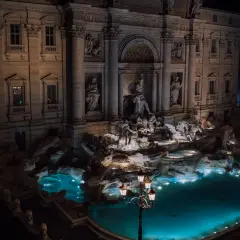 Fontana di Trevi a Roma di notte, con le sue sculture illuminate e l'acqua turchese che brilla sotto i lampioni.
