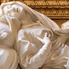 Estasi di Santa Teresa a Roma, marmo bianco su fondo dorato. La santa giace su un cuscino, con un'espressione di profonda emozione.