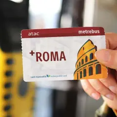 Una mano tiene una tessera metropolitana Roma con il Colosseo stilizzato. La carta è ricaricabile e riporta il logo ATAC.