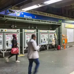 Persone acquistano biglietti alle macchinette automatiche nella stazione metro Roma EUR. Segnali indicano binari e uscite.