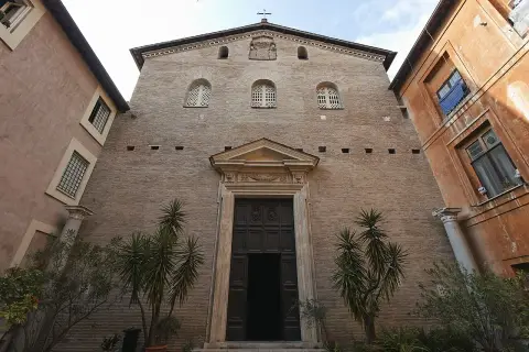 Facciata in mattoni di Santa Prassede a Roma, con un grande portale in legno e piante verdi.