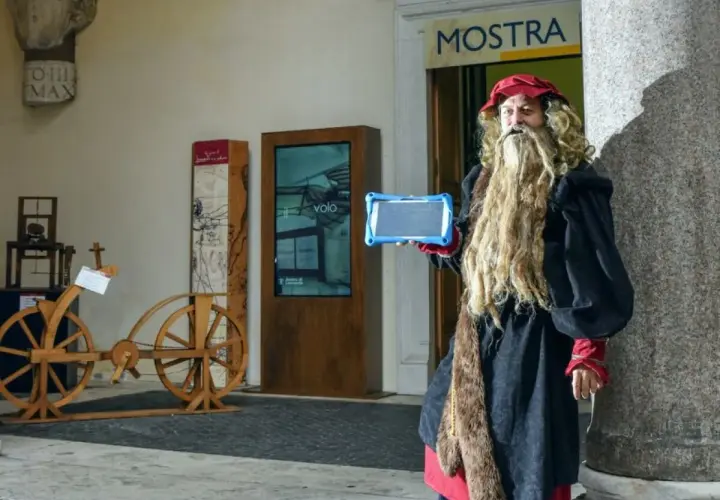 Uomo vestito da Leonardo da Vinci con tablet, pronto per una caccia al tesoro a Roma, vicino a un'antica bicicletta di legno.