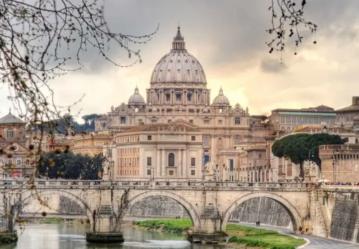 Un ponte di Roma attraversa il Tevere, con la maestosa cupola di San Pietro che domina lo skyline in una giornata invernale.