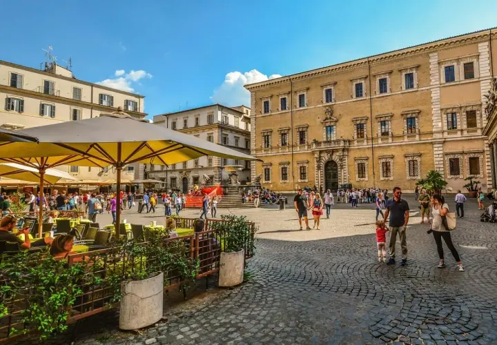Piazza animata con gente che passeggia e si gode la movida a Roma, tavolini all'aperto e palazzi storici sullo sfondo.