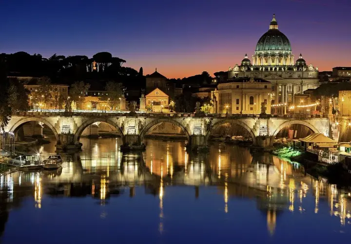 Ponte Sant'Angelo illuminato di notte, con la cupola di San Pietro sullo sfondo. Un'idea per cosa visitare a Roma in due giorni.