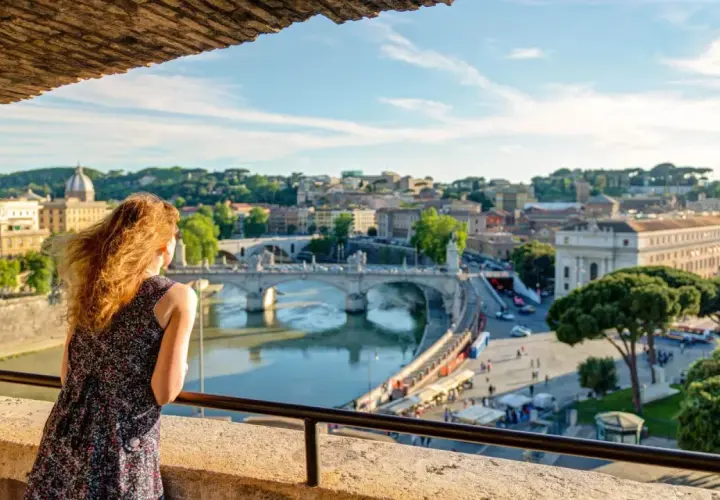 Una donna ammira il panorama di Roma con il Tevere e Ponte Sant'Angelo, un'immagine perfetta per il Ferragosto a Roma.