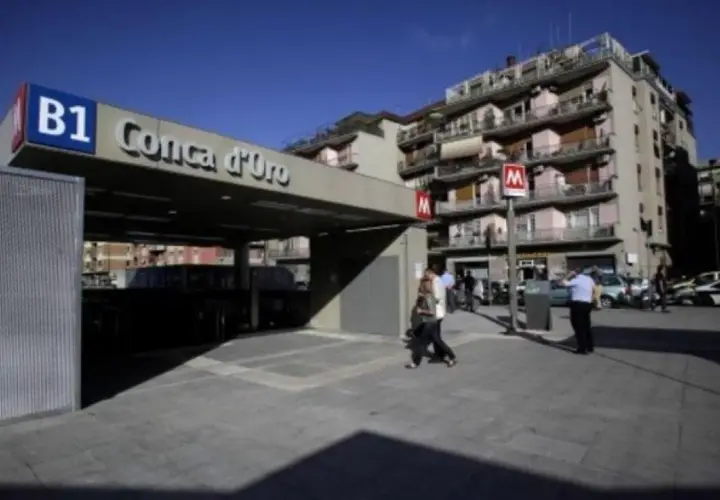 Ingresso della metro B1 Conca d'Oro a Roma, con persone che camminano e palazzi sullo sfondo.