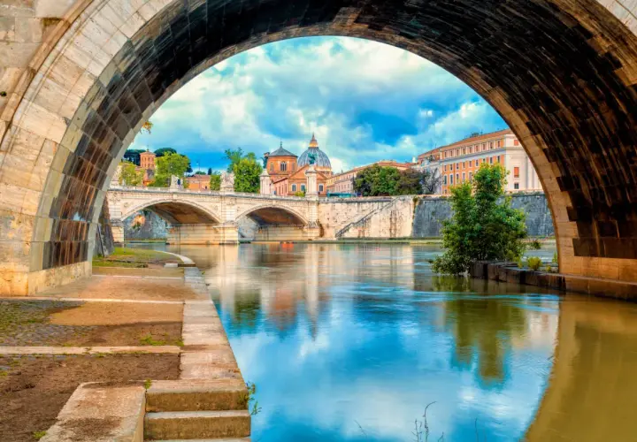 Ponte Sant'Angelo e il Tevere, un'icona di cosa vedere a Roma. La cupola di San Pietro si riflette sull'acqua.