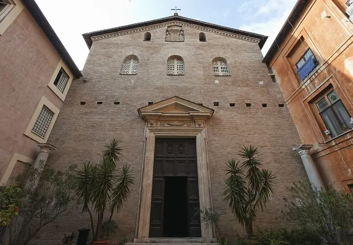 Facciata in mattoni di Santa Prassede a Roma, con un grande portale in legno e piante verdi.