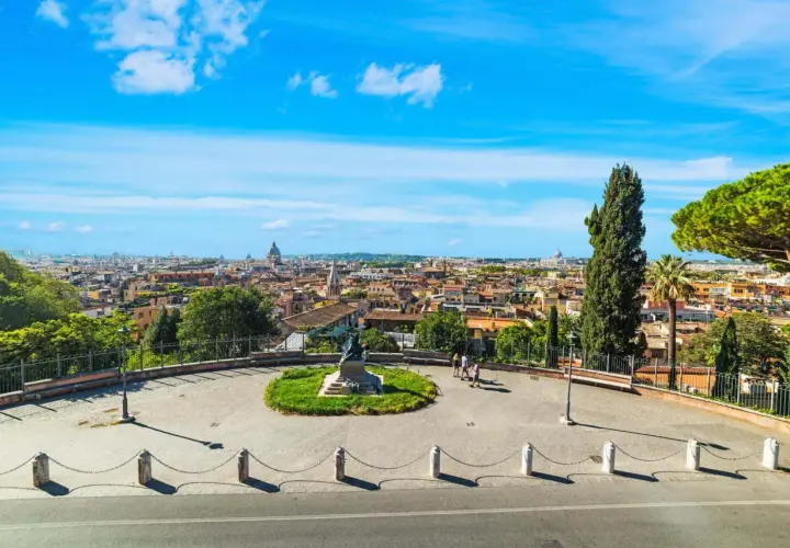 Vista panoramica di Roma con cupole e tetti, un monumento al centro e persone che passeggiano. Un'emozione da vivere a Roma gratis.