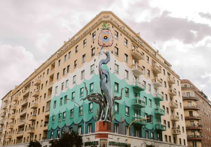 Un maestoso airone blu e tentacoli di polpo adornano un palazzo nel quartiere Ostiense, un'opera d'arte urbana che cattura lo sguardo.