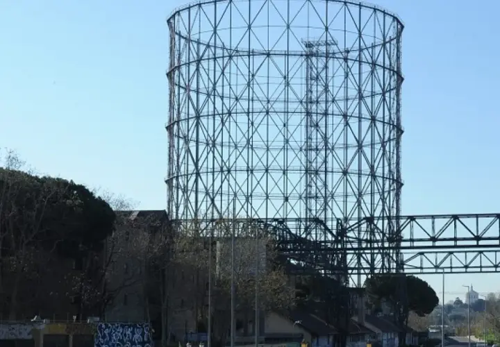 Il **gasometro Roma** si erge imponente contro il cielo azzurro, una struttura metallica iconica che domina il paesaggio urbano.